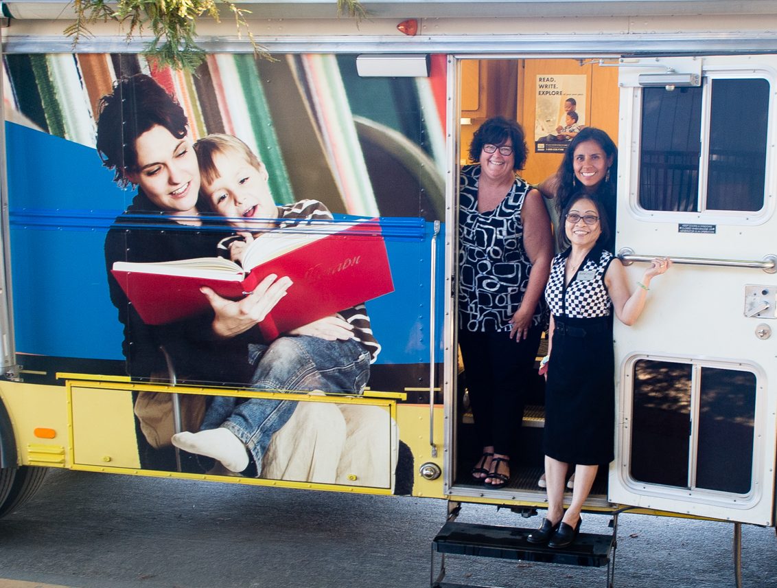 three library staff members stand at open door of book mobile