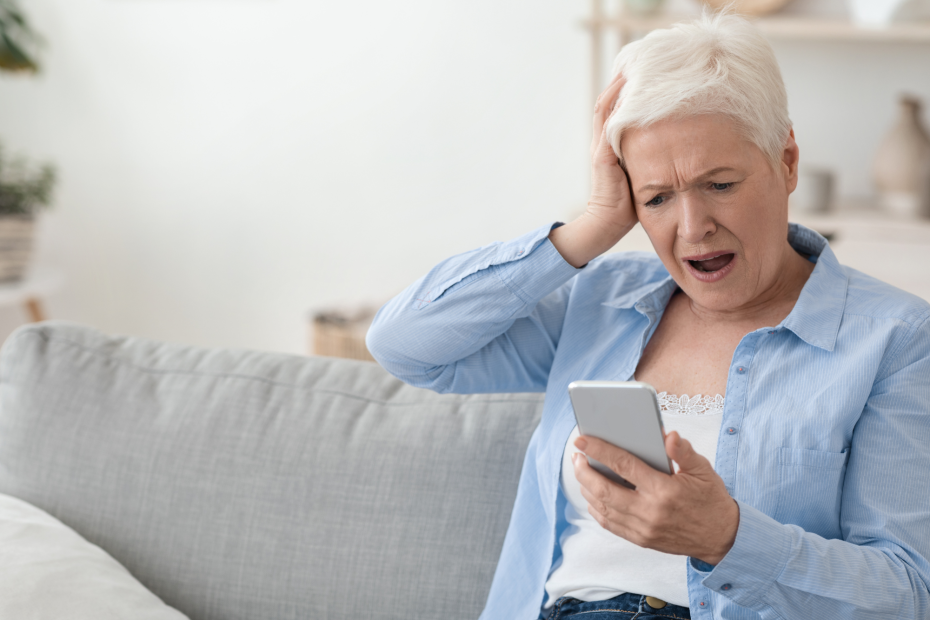 Woman sitting on couch looks at her phone with frustrated expression.