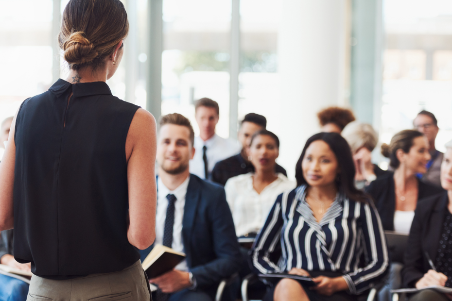 Woman stands in front of a seated audience and gives a presentation